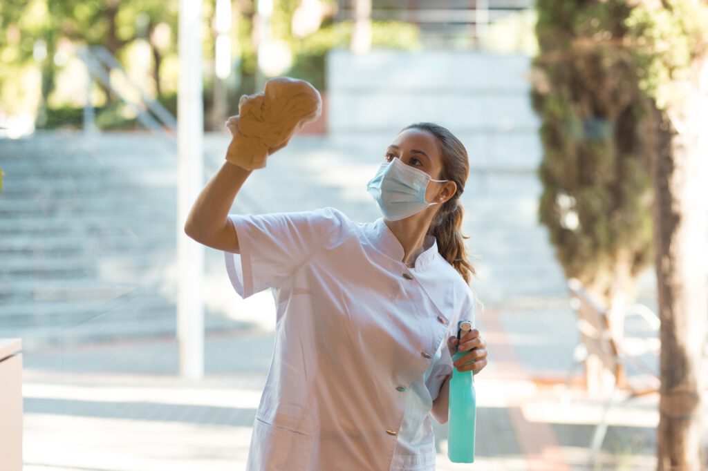 Young woman cleaning windows of clinic on outside